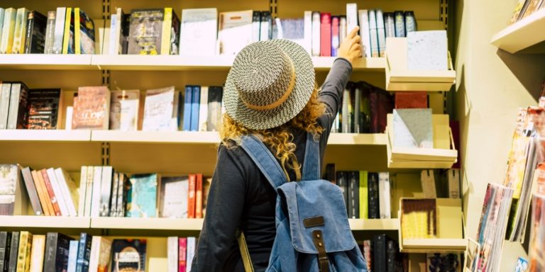 Woman in a hate picking a book off of a shelf in a bookstore