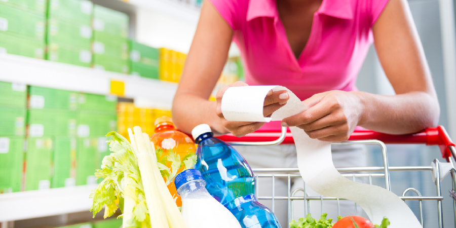 Smiling young woman holding a long grocery receipt at supermarket.