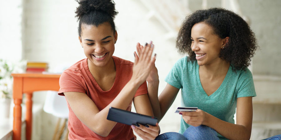 Two cheerful mixed race curly girlfriends shopping online with tablet computer and credit card at home Two cheerful mixed race curly girlfriends shopping online with tablet computer and credit card at home
