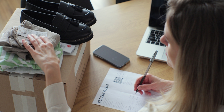 Woman filling out a return form next to a package with clothes and shoes on top