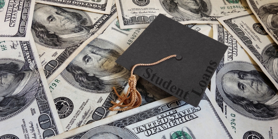 A graduation cap that says "student loans" on top of a pile of money