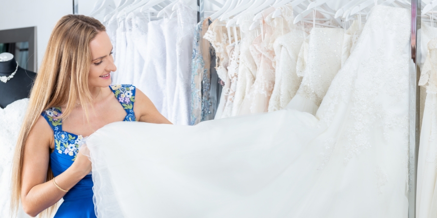 Woman holding the bottom of a wedding dress next to a rack of dresses